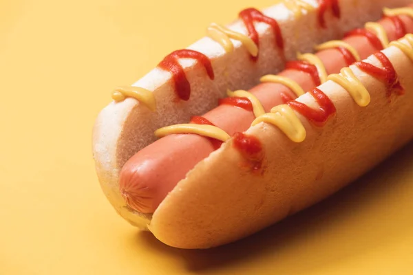 Nahaufnahme von köstlichem Hot Dog mit Wurst, Senf und Ketchup auf gelb — Stockfoto