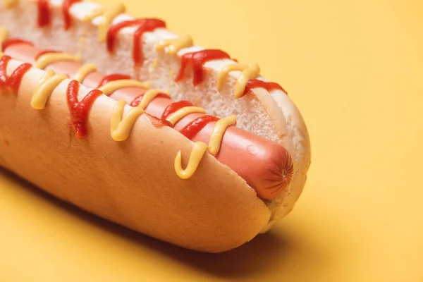 Close up of one hot dog with sausage, mustard and ketchup on yellow — Stock Photo