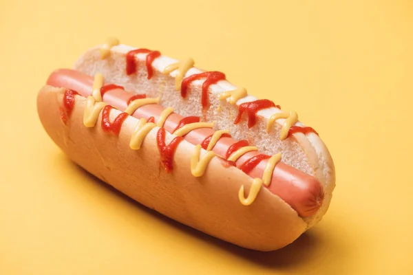 Primer plano de sabroso perrito caliente con salchicha, mostaza y ketchup en amarillo - foto de stock