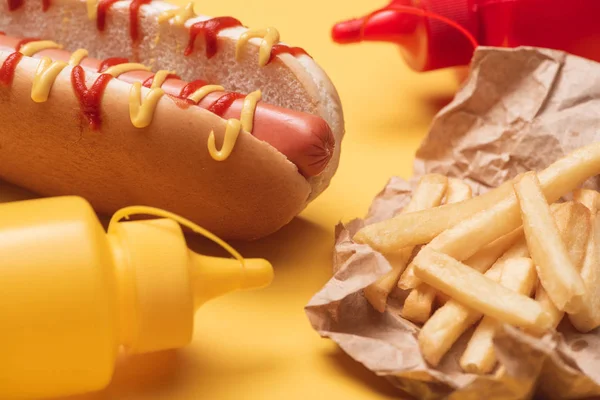 Tasty hot dog, french fries in paper and bottles with ketchup and mustard on yellow — Stock Photo