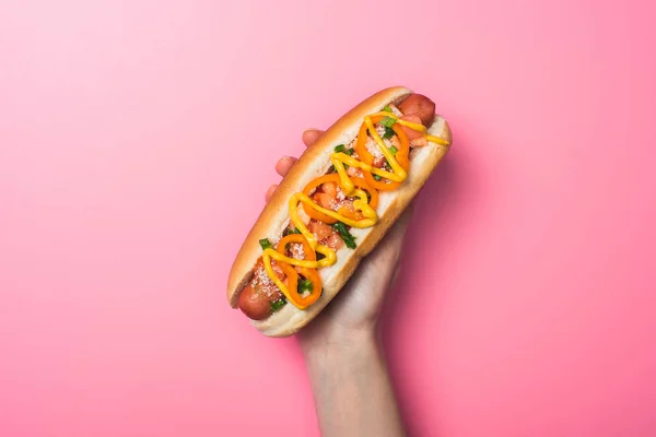Cropped view of woman holding delicious hot dog on pink — Stock Photo