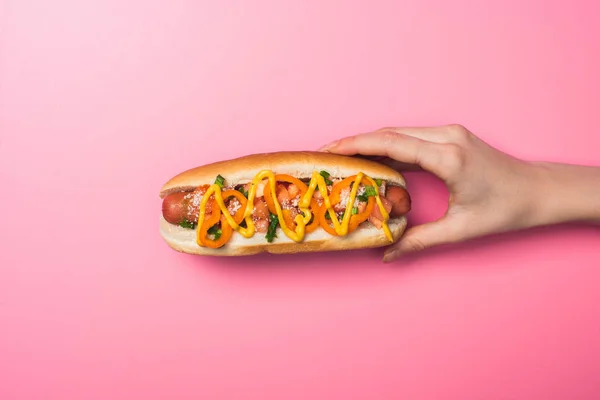 Cropped view of woman holding tasty hot dog with mustard on pink — Stock Photo