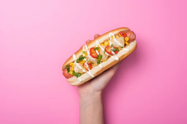 Cropped view of woman holding delicious hot dog on pink — Stock Photo