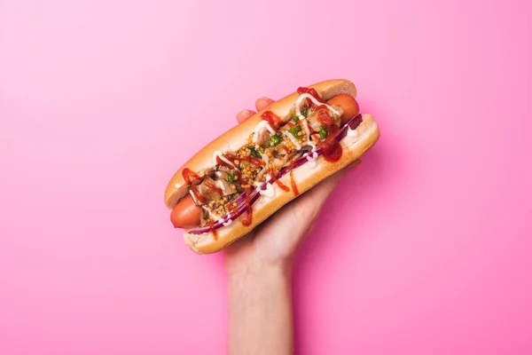 Partial view of woman holding yummy hot dog in hand on pink — Stock Photo