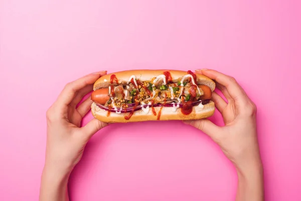 Cropped view of woman holding tasty hot dog in hands on pink — Stock Photo