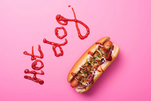 Vista superior de un hot dog en rosa con palabra hot dog escrita con ketchup - foto de stock
