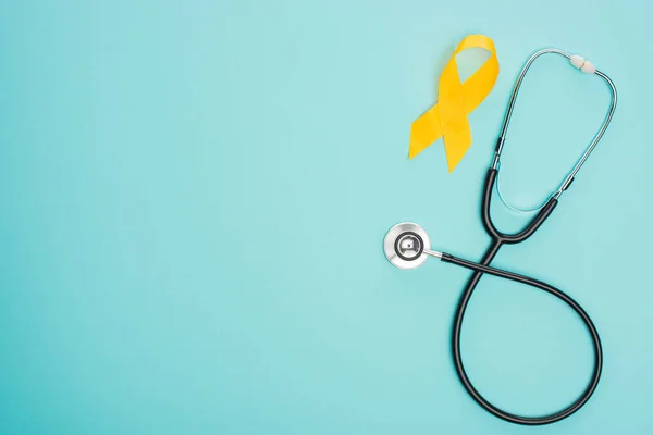 Top view of yellow ribbon with stethoscope on blue background, international childhood cancer day concept — Stock Photo