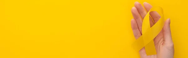 Частковий вигляд жіночої руки з жовтою стрічкою на барвистому фоні, панорамний знімок, концепція міжнародного дня дитячого раку — Stock Photo
