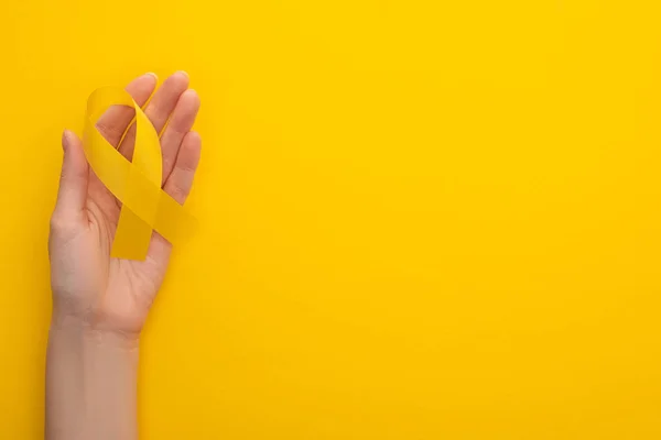 Partielle Ansicht der weiblichen Hand mit gelbem Band auf buntem Hintergrund, Konzept zum internationalen Kinderkrebstag — Stockfoto