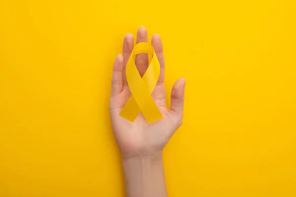 Vue recadrée de la main féminine avec ruban de sensibilisation jaune sur fond coloré, concept de journée internationale contre le cancer chez l'enfant — Photo de stock