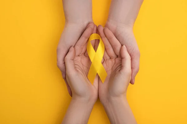 Vista recortada de pareja sosteniendo cinta amarilla sobre fondo colorido, concepto de día internacional del cáncer infantil — Stock Photo