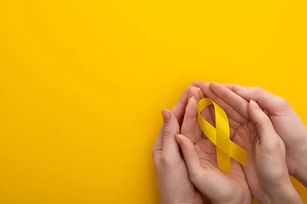 Vista recortada de la mujer y el hombre sosteniendo cinta amarilla sobre fondo colorido, concepto de día del cáncer infantil internacional - foto de stock