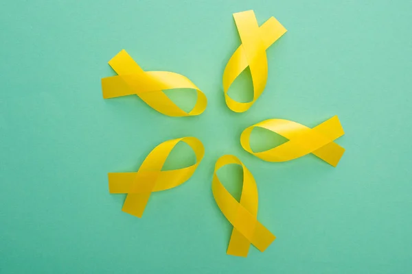 Vista superior de las cintas de conciencia amarillas sobre fondo turquesa, concepto del día internacional del cáncer infantil - foto de stock