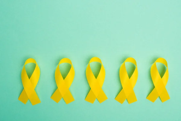 Flache Lage mit gelben Bewusstseinsbändern auf türkisfarbenem Hintergrund, Konzept zum internationalen Kinderkrebstag — Stockfoto