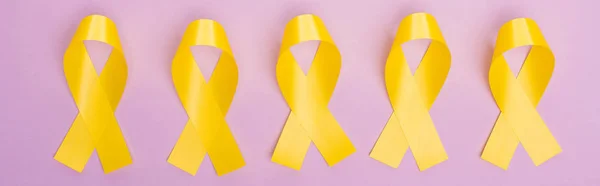 Acostado plano con cintas de conciencia amarillas sobre fondo violeta, plano panorámico, concepto de día internacional del cáncer infantil - foto de stock