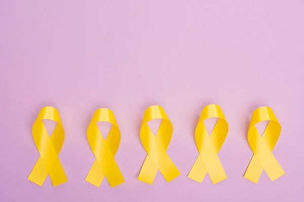 Flat lay with yellow awareness ribbons on violet, international childhood cancer day concept — Stock Photo