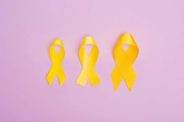 Top view of yellow awareness ribbons on violet background, international childhood cancer day concept — Stock Photo