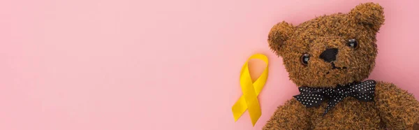 Draufsicht auf gelbes Band und Teddybär auf rosa Hintergrund, Panoramaaufnahme, Konzept zum internationalen Kinderkrebstag — Stockfoto