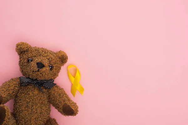 Vue du dessus du ruban jaune près de l'ours en peluche sur fond rose, concept de journée internationale contre le cancer chez les enfants — Photo de stock
