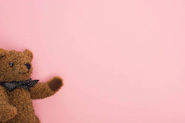 Vista superior del osito de peluche marrón con lazo sobre fondo rosa - foto de stock