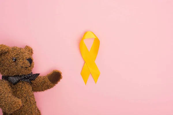 Vista superior de cinta amarilla y juguete sobre fondo rosa, concepto del día internacional del cáncer infantil - foto de stock