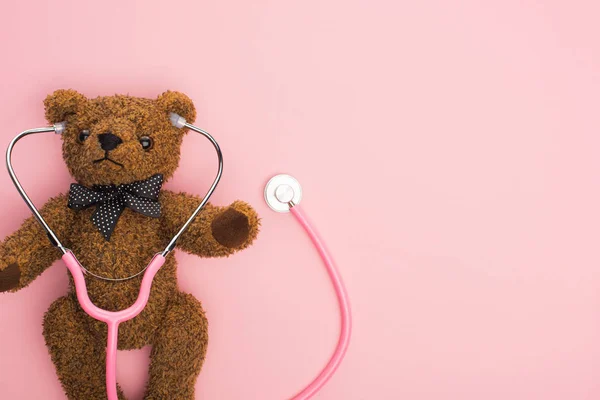 Vista superior del estetoscopio con oso de peluche sobre fondo rosa, concepto de día internacional del cáncer infantil - foto de stock