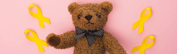 Draufsicht auf gelbe Bänder und Teddybär auf rosa Hintergrund, Panoramaaufnahme, Konzept zum internationalen Kinderkrebstag — Stockfoto