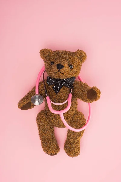 Vue du dessus de l'ours en peluche brun avec stéthoscope sur rose, concept de journée internationale contre le cancer chez l'enfant — Photo de stock