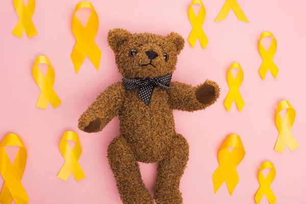 Draufsicht auf gelbe Bänder um Teddybär auf rosa Hintergrund, Konzept zum internationalen Kinderkrebstag — Stockfoto