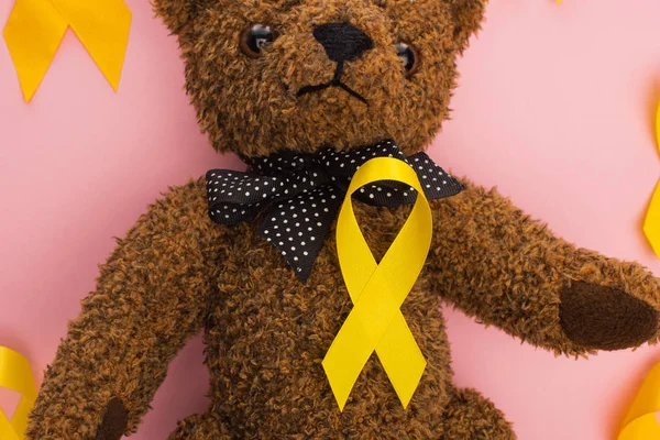 Vue du dessus des rubans jaunes avec ours en peluche sur fond rose, concept de journée internationale contre le cancer chez les enfants — Photo de stock