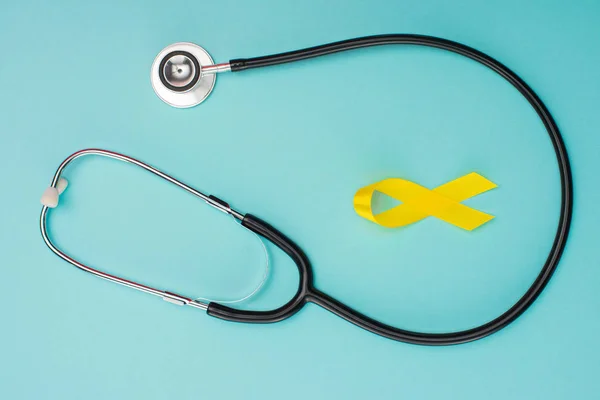 Vista superior de la cinta amarilla de la conciencia y del estetoscopio en el fondo azul, concepto internacional del día del cáncer de la niñez - foto de stock