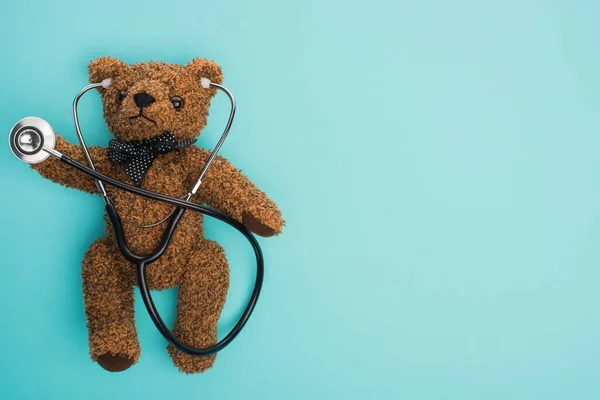 Vista superior del oso de peluche marrón con estetoscopio sobre fondo azul, concepto de día internacional del cáncer infantil - foto de stock