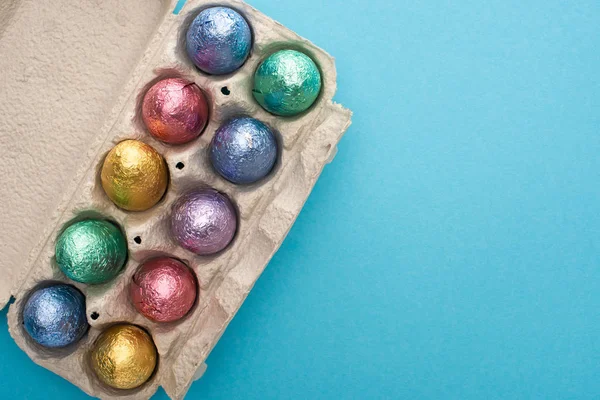 Vista superior de huevos de Pascua de chocolate en bandeja de huevo sobre fondo azul - foto de stock