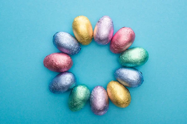 Vista superior del círculo con huevos de Pascua de chocolate en lámina de colores sobre fondo azul - foto de stock