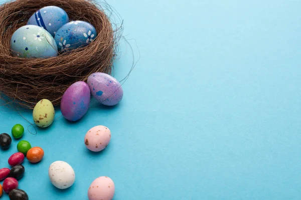 Nido con uova di Pasqua e caramelle colorate su sfondo blu — Foto stock