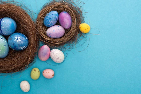 Вид зверху на барвисті великодні яйця в гніздах на синьому фоні — стокове фото