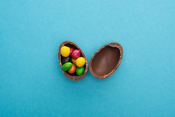 Top view of chocolate Easter egg halves with colorful sweets on blue background — Stock Photo