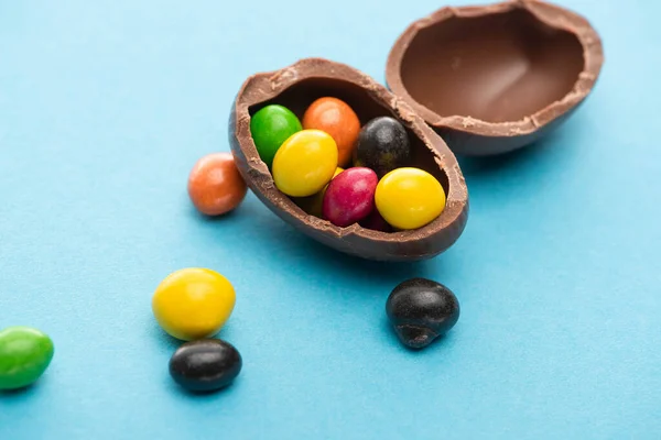 Close up view of chocolate Easter egg halves with colorful sweets on blue background — Stock Photo