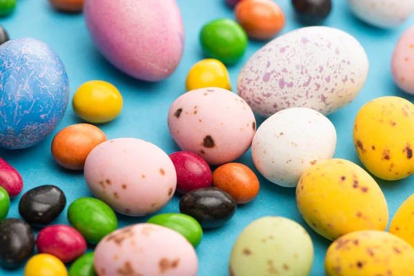 Selective focus of bright colorful sweets and easter eggs on blue background — Stock Photo