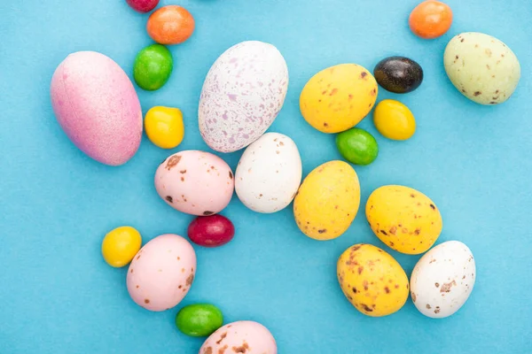 Vista superior de dulces de colores brillantes y huevos de Pascua sobre fondo azul - foto de stock