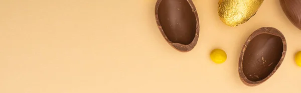 Верхний вид шоколадных яиц с желтыми сладостями на бежевом фоне, панорамный снимок — стоковое фото