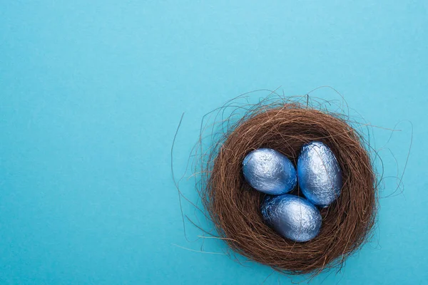 Vista superior de huevos de Pascua de chocolate dentro del nido sobre fondo azul - foto de stock