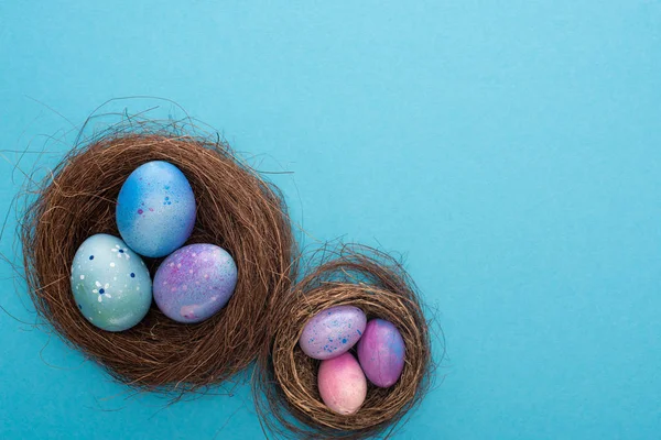 Vista superior de huevos de Pascua en nidos sobre fondo azul - foto de stock