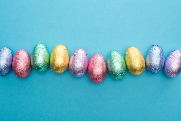 Vista superior de ovos de Páscoa de chocolate em folha colorida no fundo azul — Fotografia de Stock