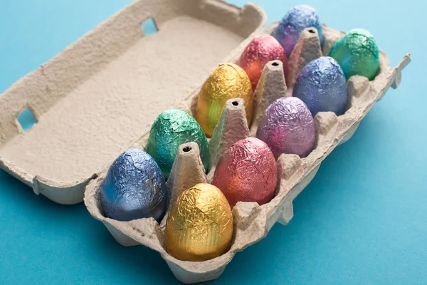 Шоколадні великодні яйця в барвистій фользі в яєчному лотку на синьому фоні — стокове фото