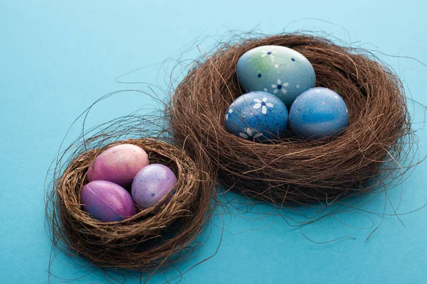 Nests with painted chicken and quail eggs on blue background — Stock Photo
