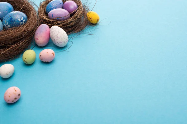 Nests with painted colorful chicken and quail eggs on blue background — Stock Photo