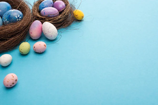 Anida con coloridos huevos pintados de pollo y codorniz sobre fondo azul - foto de stock