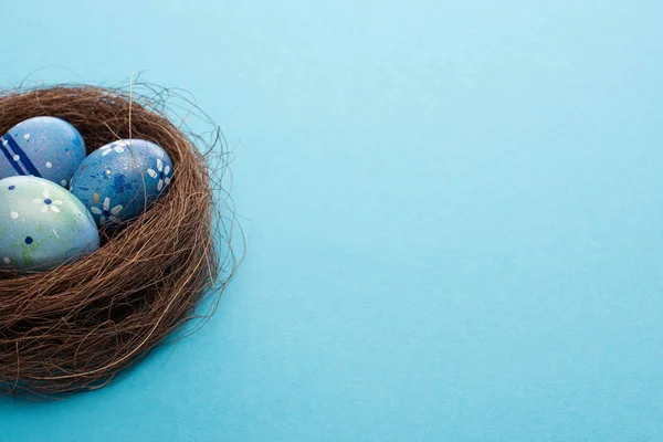 Nest with painted chicken eggs on blue background — Stock Photo