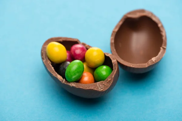 Close up view of chocolate Easter egg halves with candies on blue background — Stock Photo